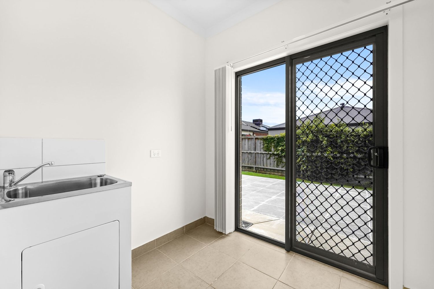 Modern laundry room with stainless steel sink and glass sliding door with security screen leading to outdoor area.