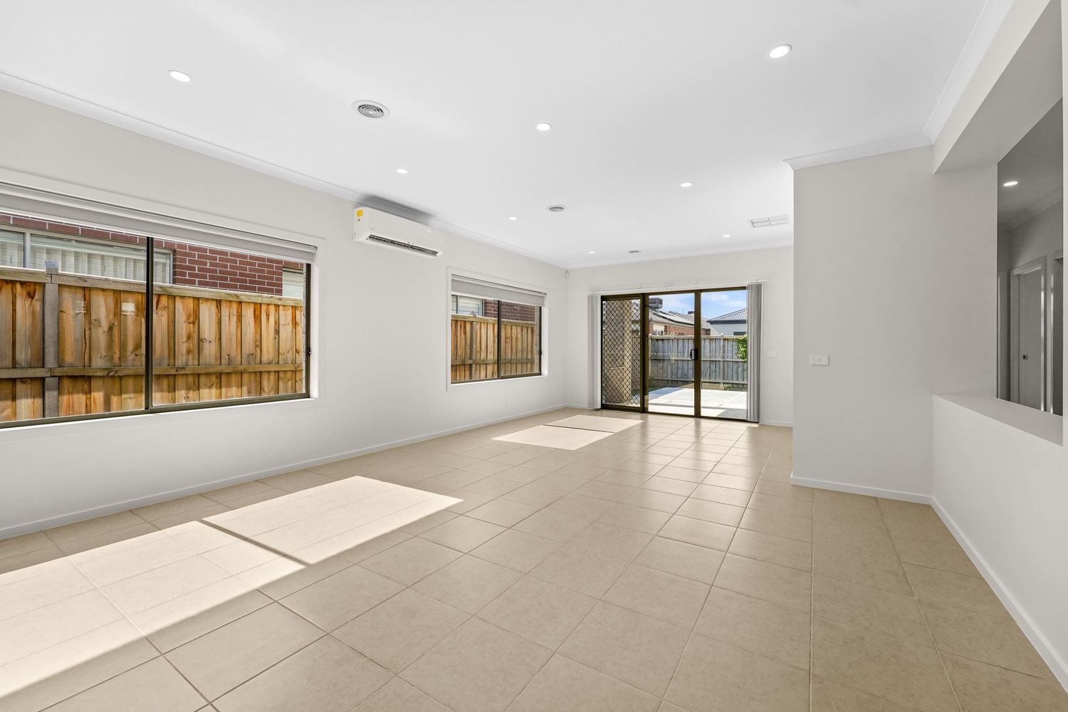 Spacious empty living room with tiled floors, sliding glass doors, and natural light streaming through bamboo privacy screens.