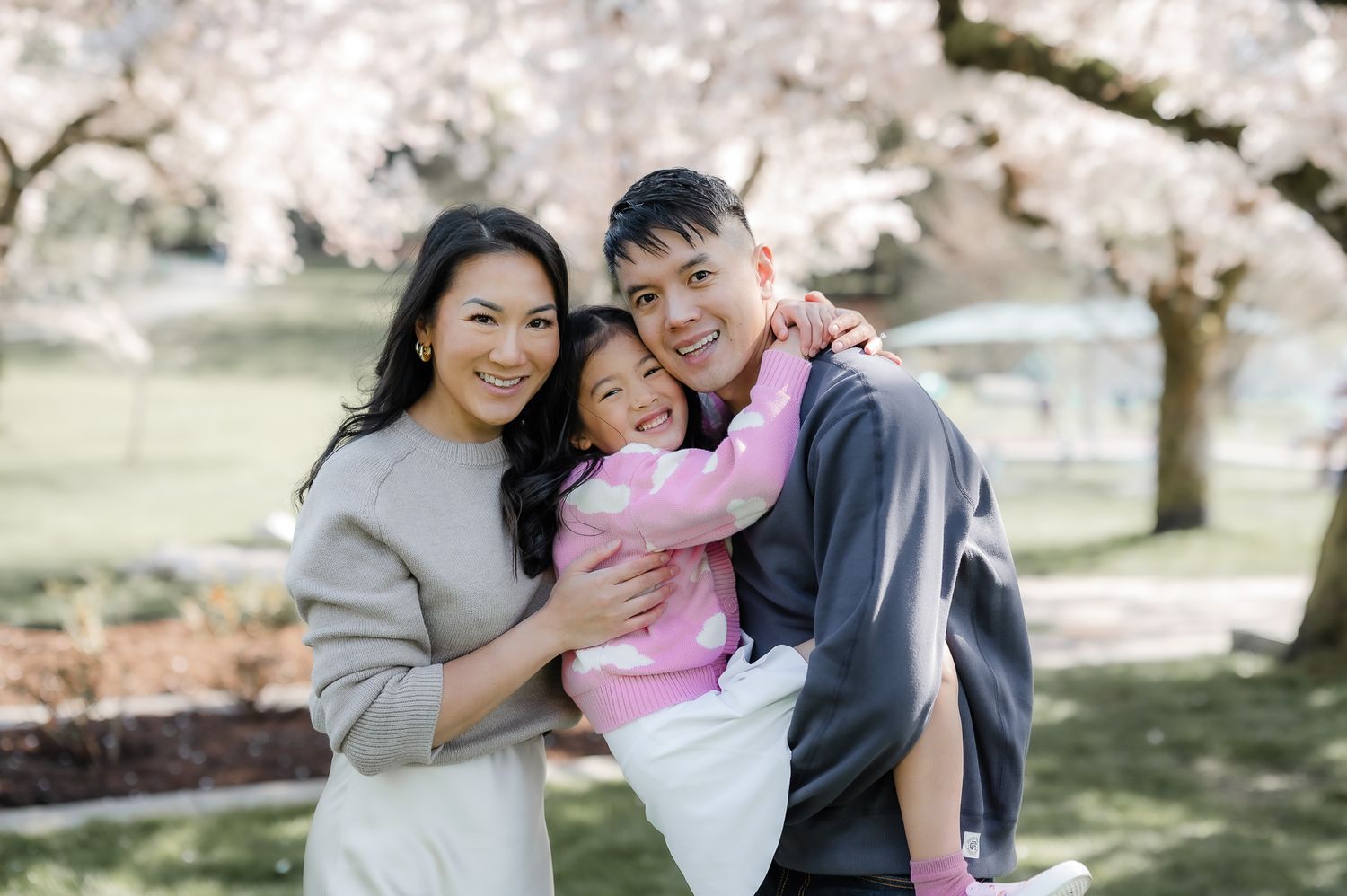 A happy family stands together under blooming cherry trees on a spring day at the park.