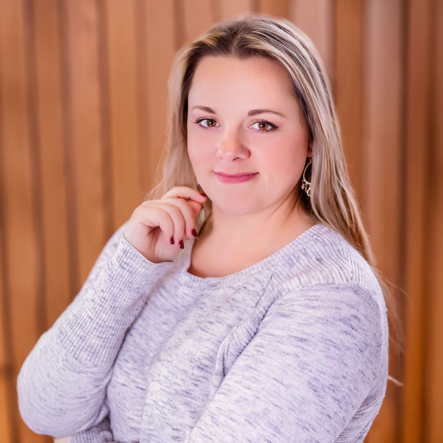 Professional portrait of a person in light gray sweater sitting against a wood paneled backdrop.