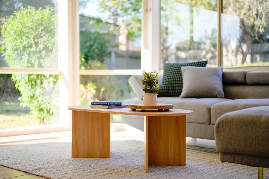 Modern living room with wooden coffee table, grey sectional sofa, and natural light streaming through windows.