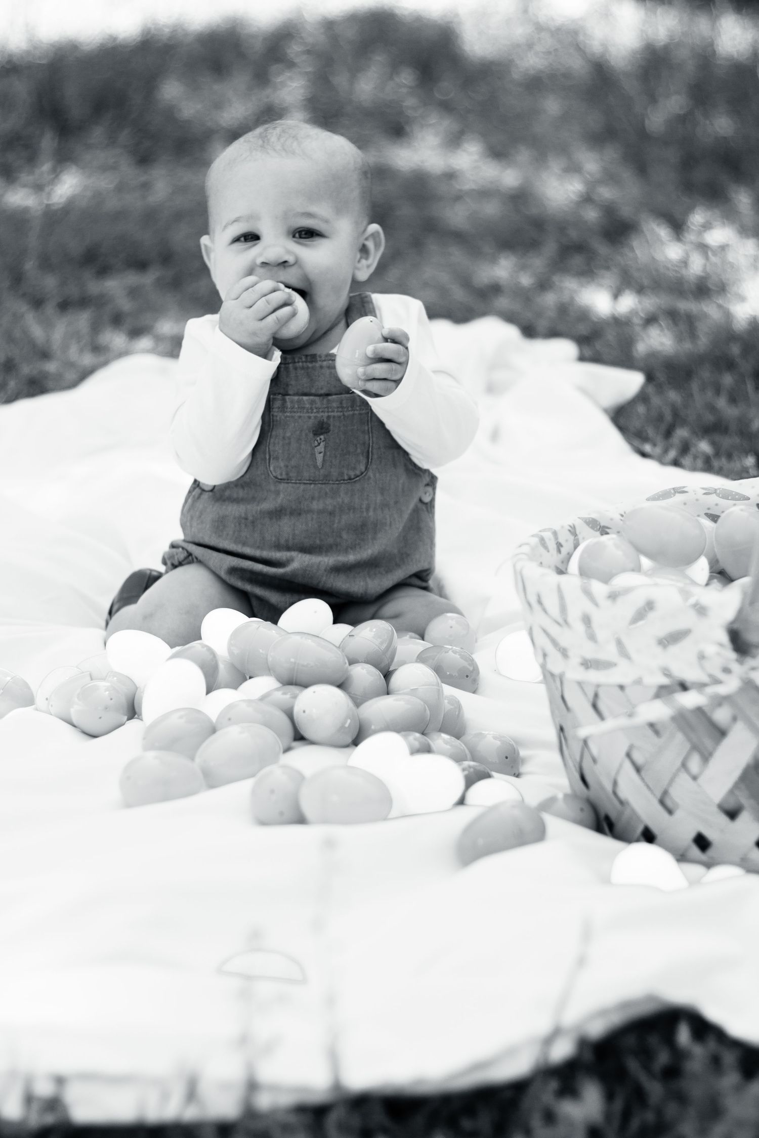 Black and white vintage photo of a small child in overalls sitting on a blanket with oranges and a basket.