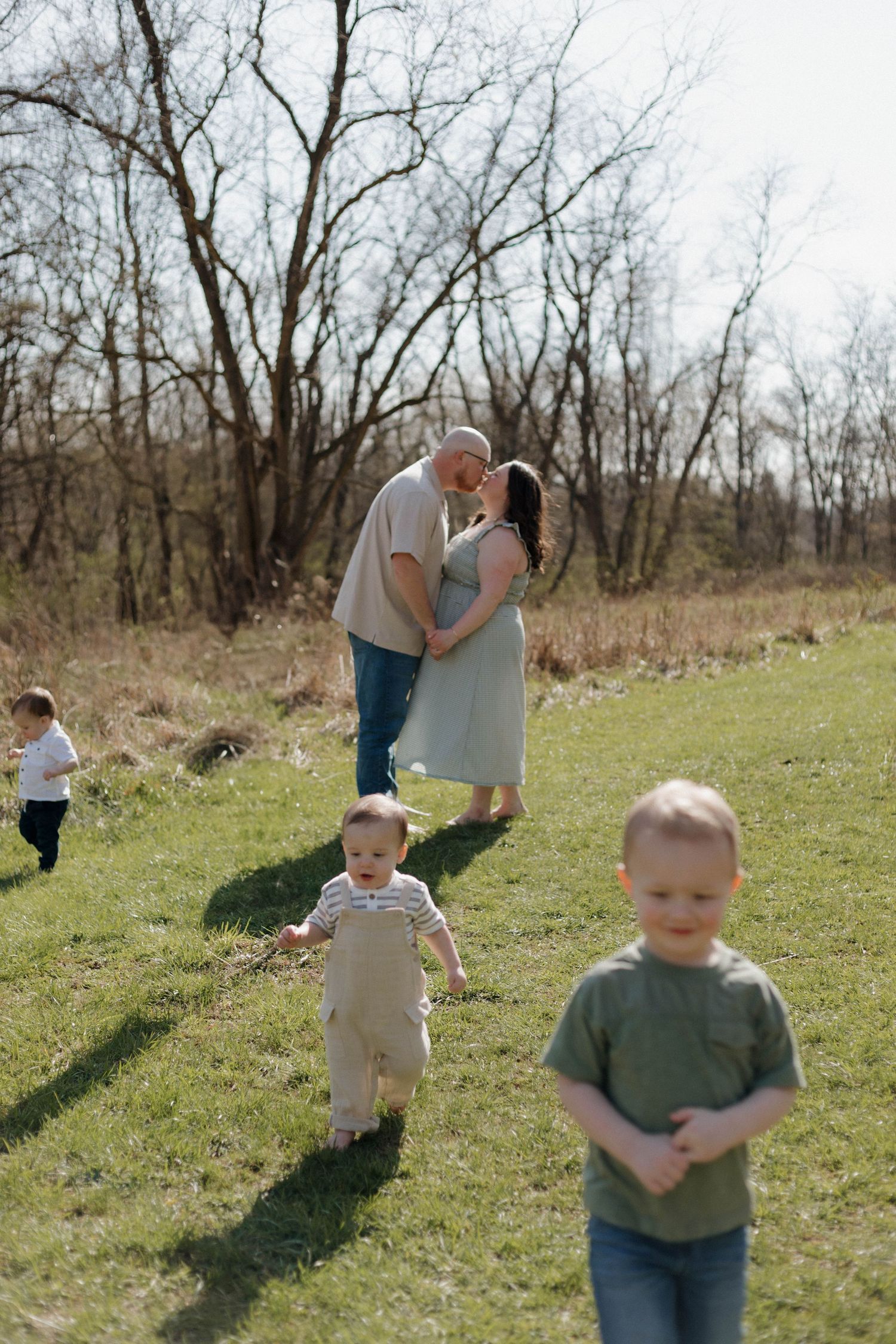 Candid family portrait in a spring meadow with children playing in the foreground on a sunny afternoon.