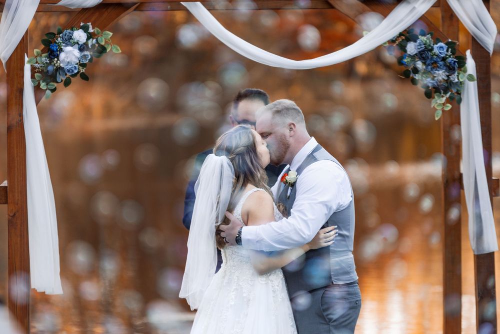 Romantic wedding kiss under decorated arch with white draping.
