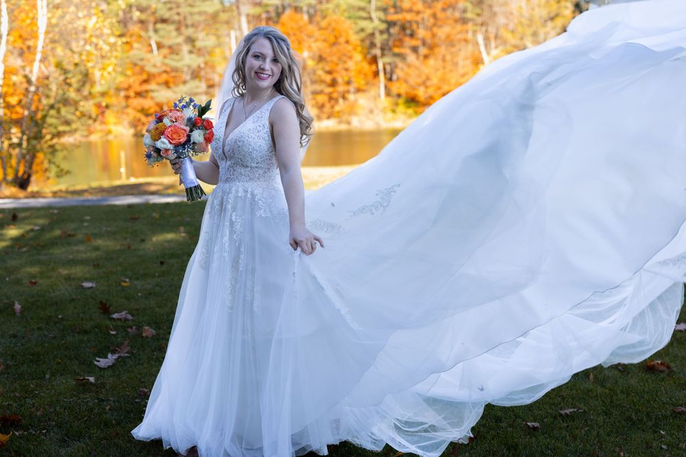 Bride in flowing white dress holding bouquet against autumn landscape background.