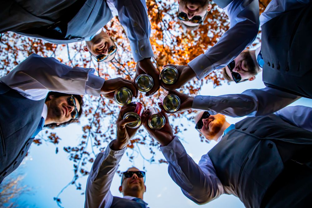 Circle of wedding party members holding flowers viewed from below against autumn trees.