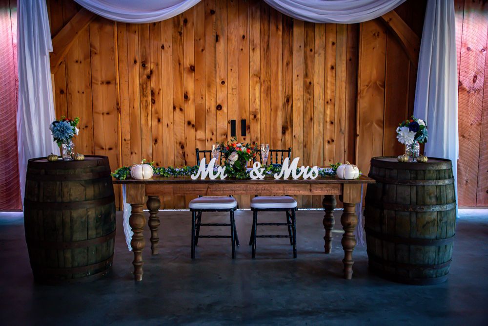 Rustic wedding reception head table with wooden barrels and Mr & Mrs sign.