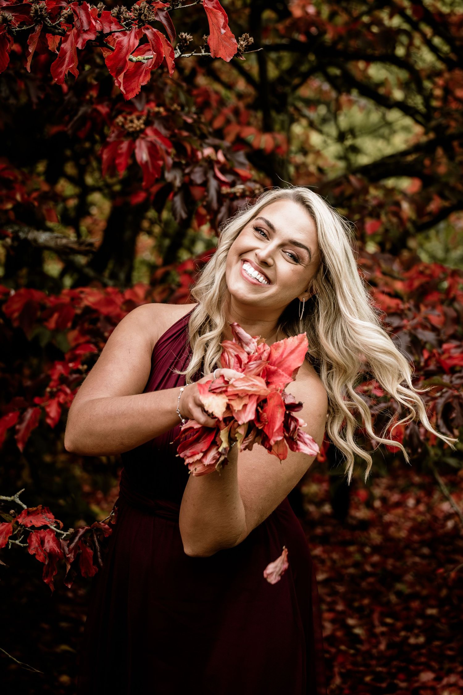 Playful autumn portrait with red maple leaves and natural lighting.