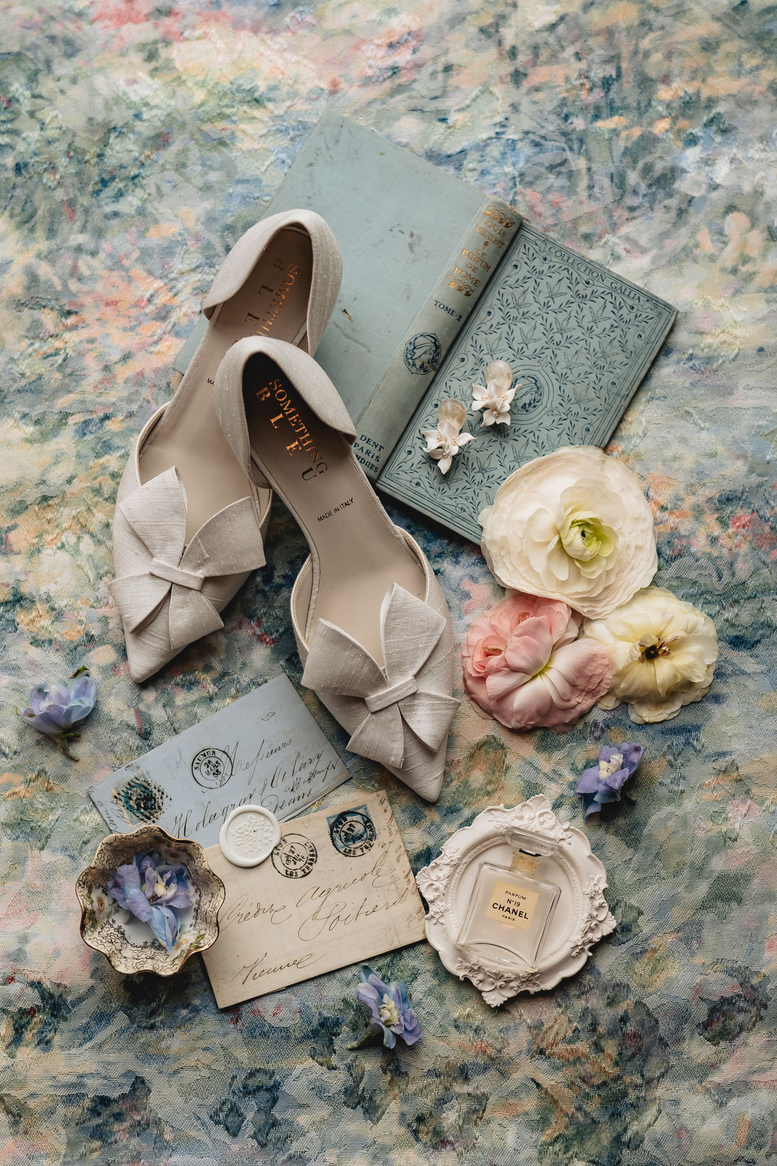 Elegant beige bridal shoes with bows styled with vintage letters, perfume jar, and soft pink and white flowers.