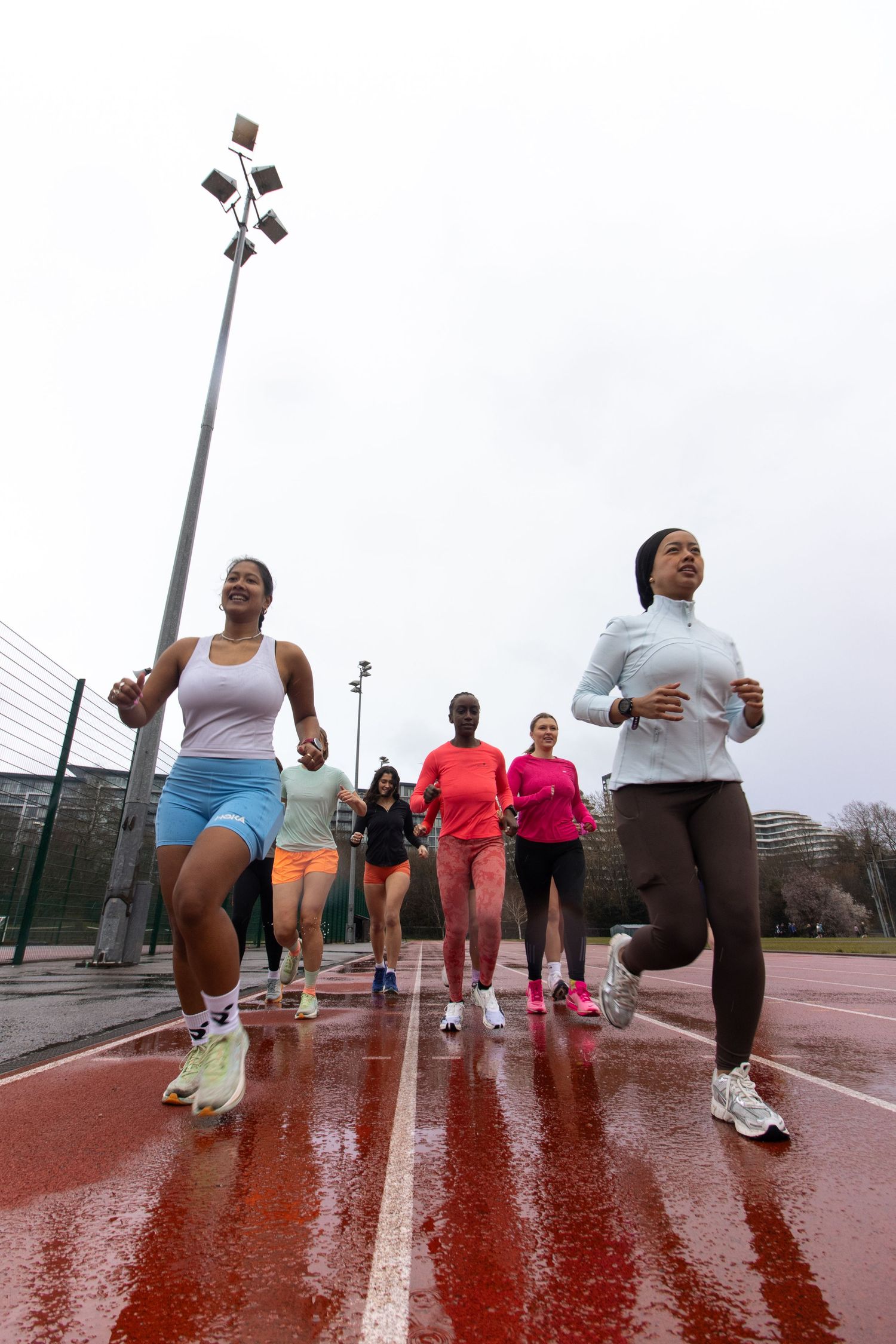 Group of female runners training together on wet track during cloudy weather.