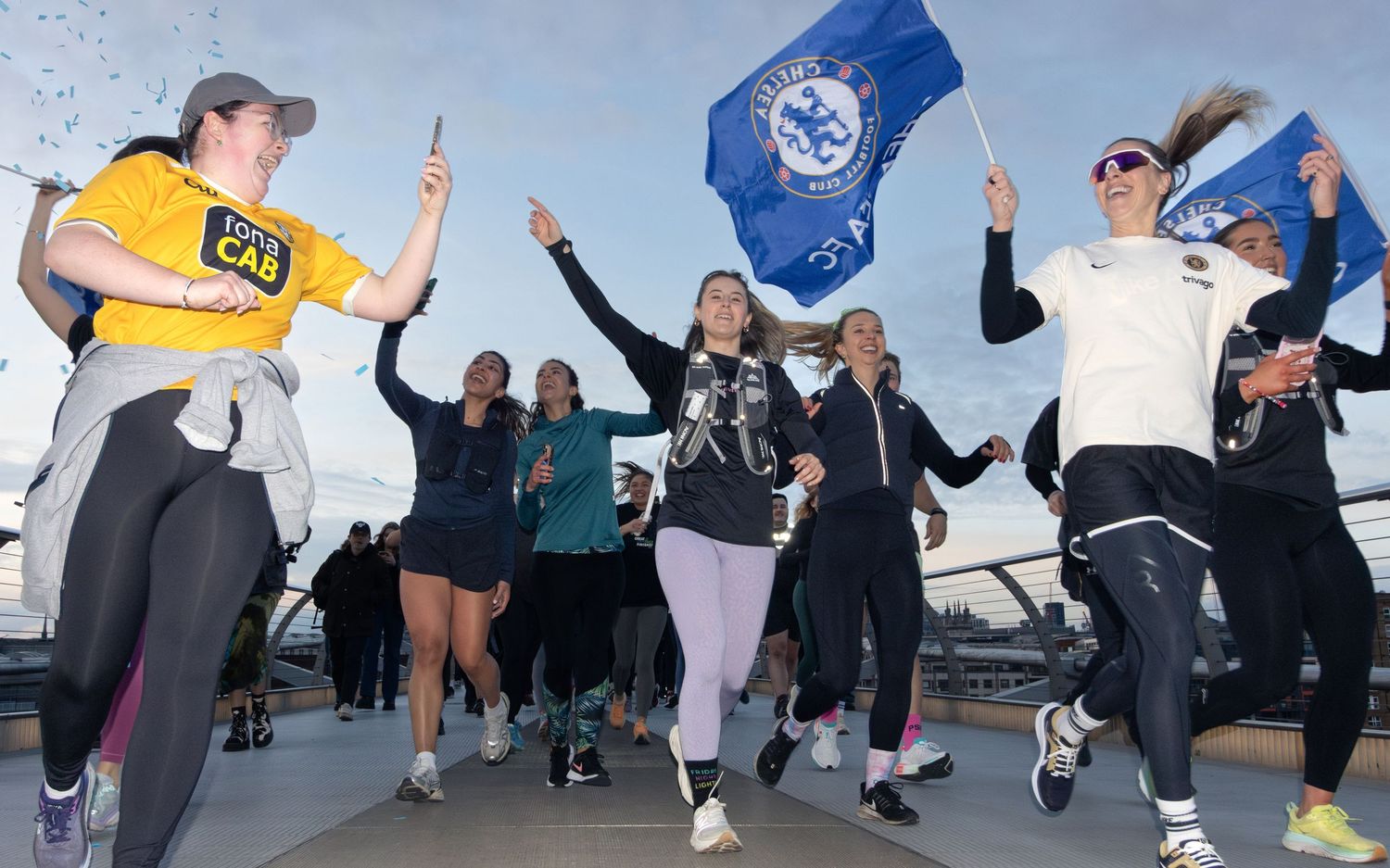 Group of enthusiastic runners celebrating with flags and confetti at outdoor event.