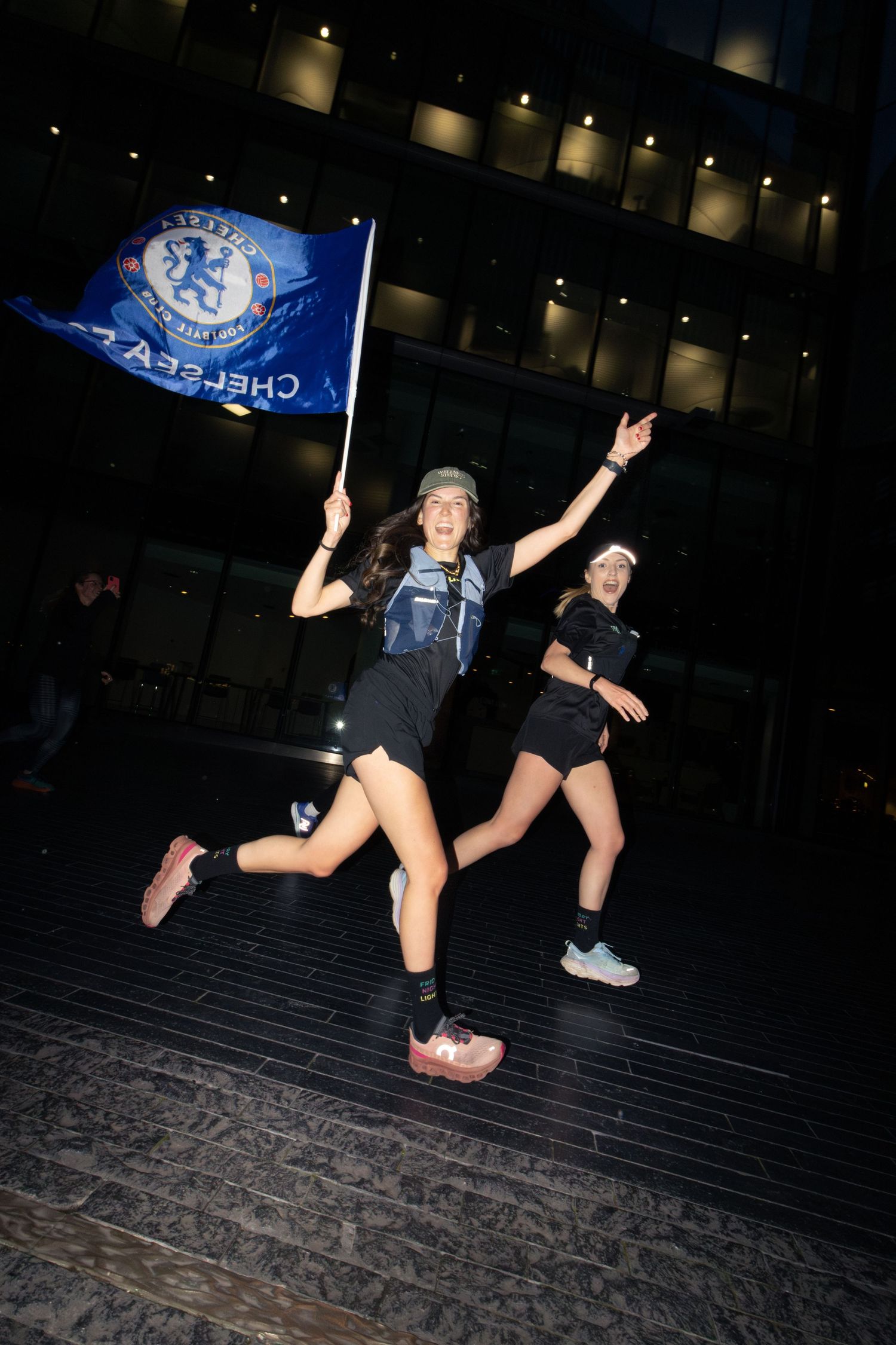 Runner jumping while waving Chelsea flag during night time celebration.