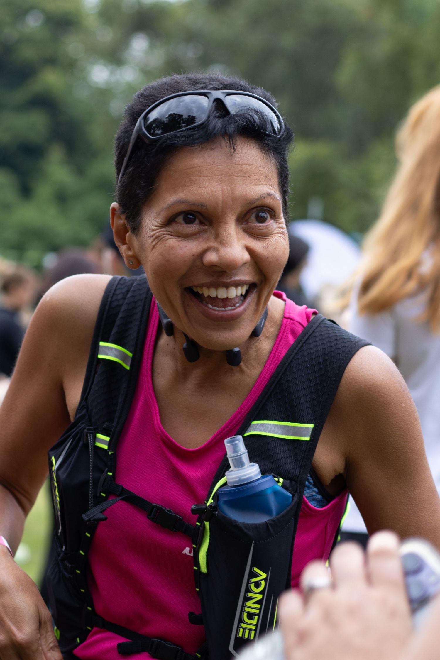Runner smiling wearing pink tank top and hydration pack during outdoor event.