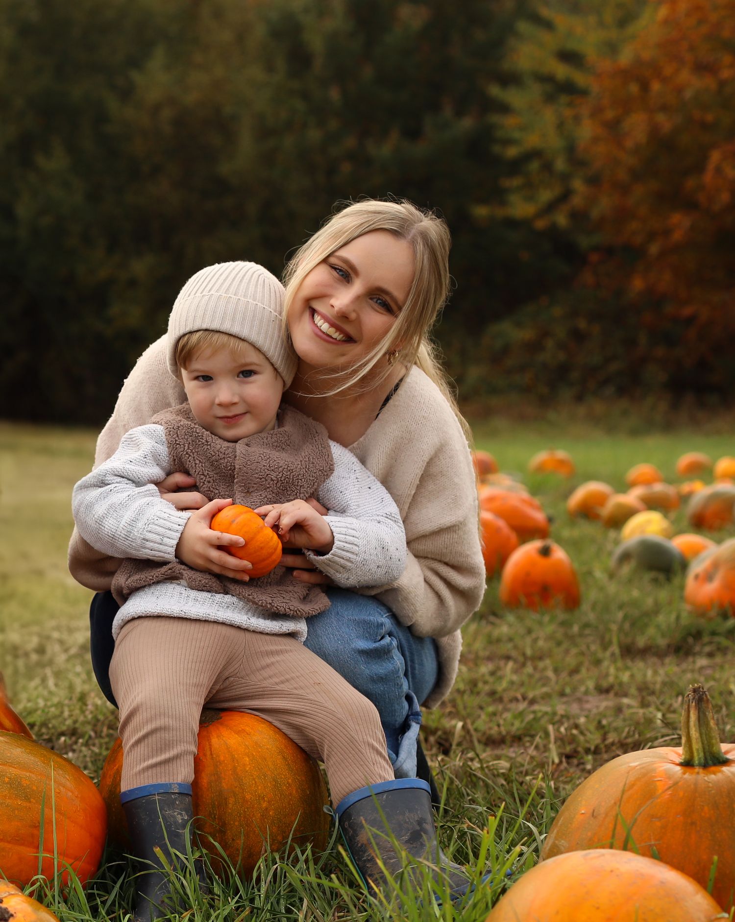 Mother and young child enjoy autumn fun sitting on pumpkins at a rustic pumpkin patch during fall harvest season.