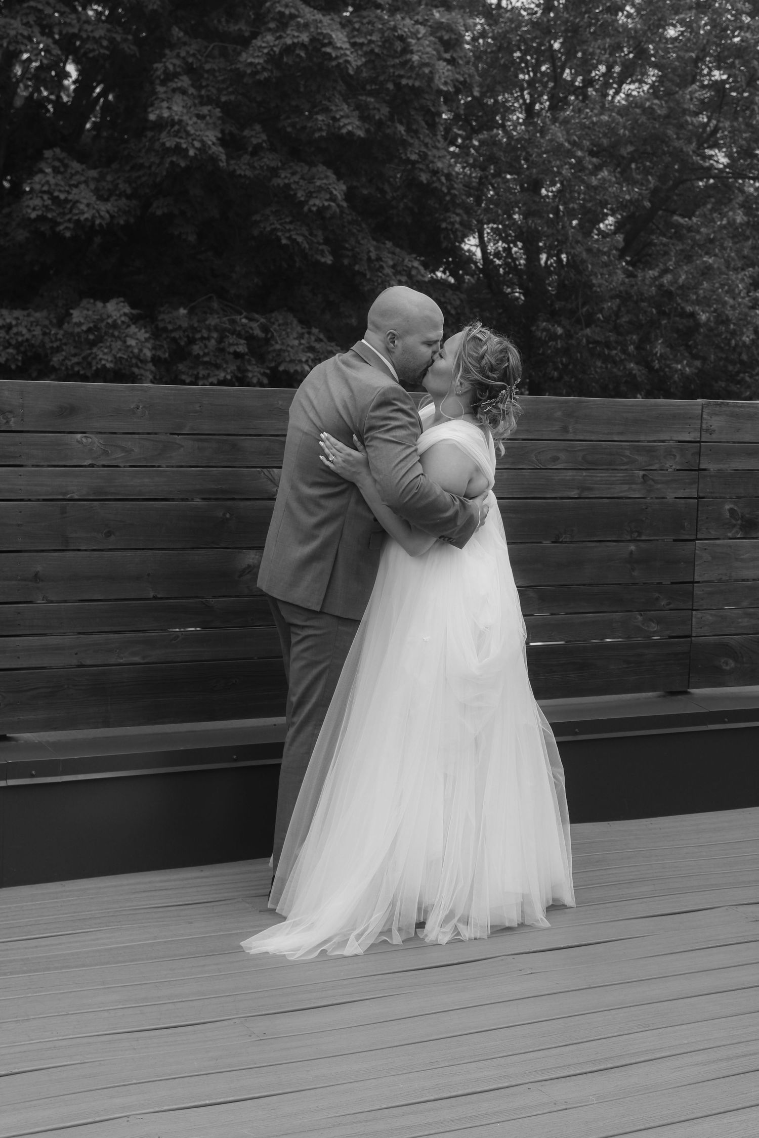 Black and white portrait of newlyweds embracing in front of a wooden wall outdoors.