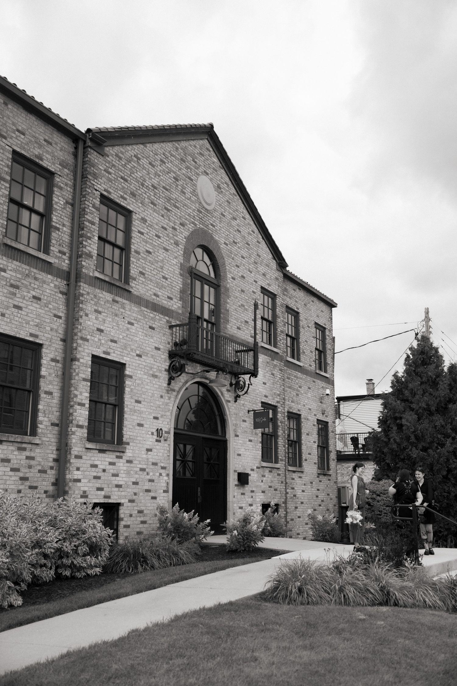 Black and white photograph of a historic brick building with arched doorway and ornate balcony detail.