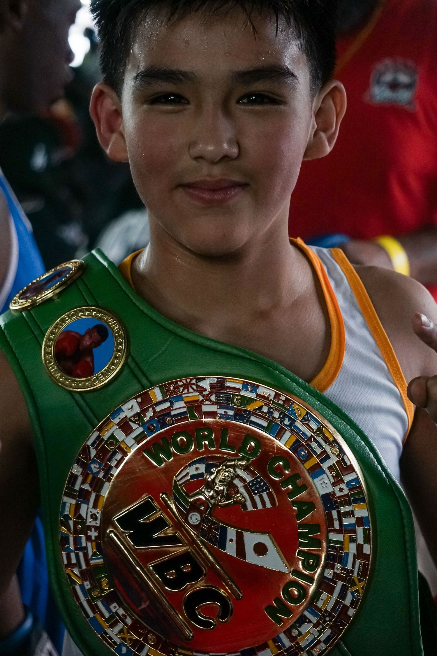 A young boxer poses with a championship belt featuring intricate martial arts designs and emblems.