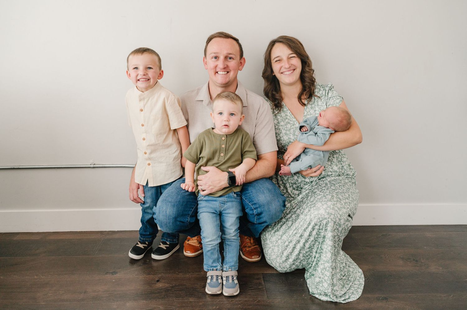 A family sits together on a bench against a light gray wall.