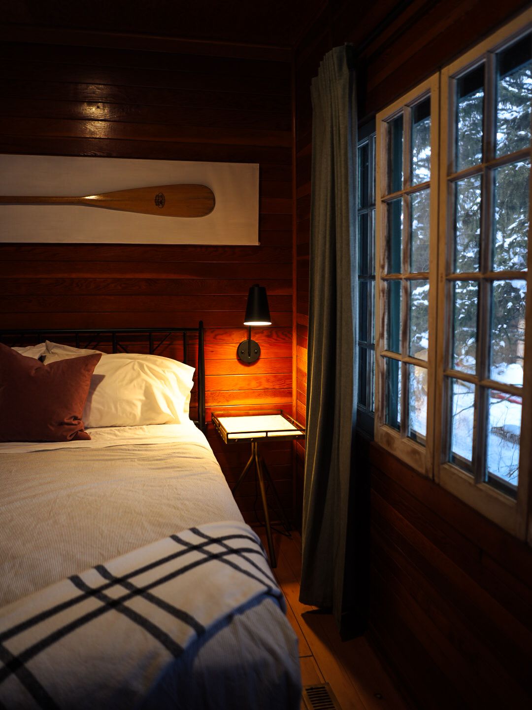 Cozy cabin bedroom interior with warm lighting and snow visible through windows.