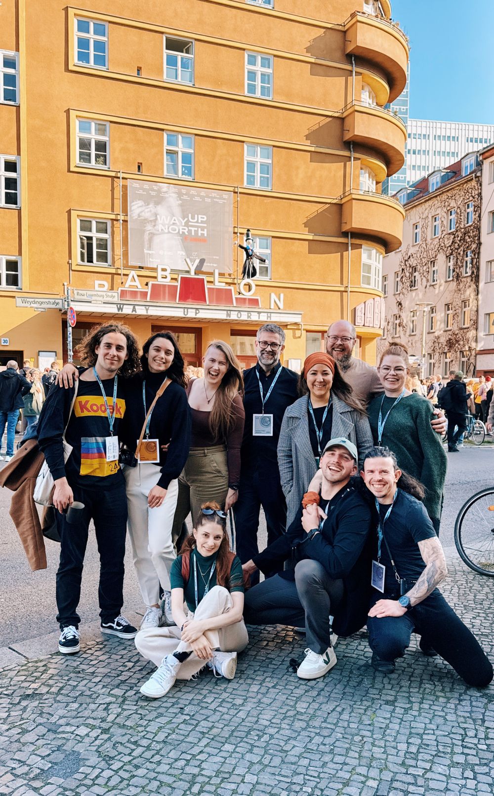 A group gathers for a photo outside a tan-colored building with curved balconies in an urban setting.