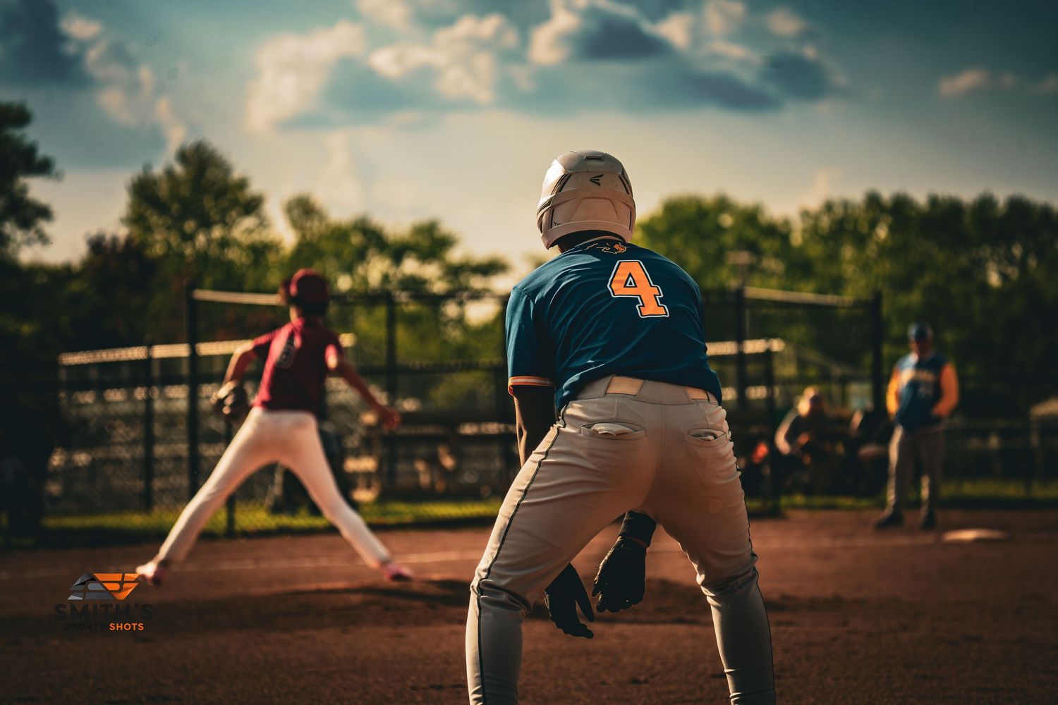 Softball player in blue and white uniform fielding a ground ball on dirt infield during daytime game.