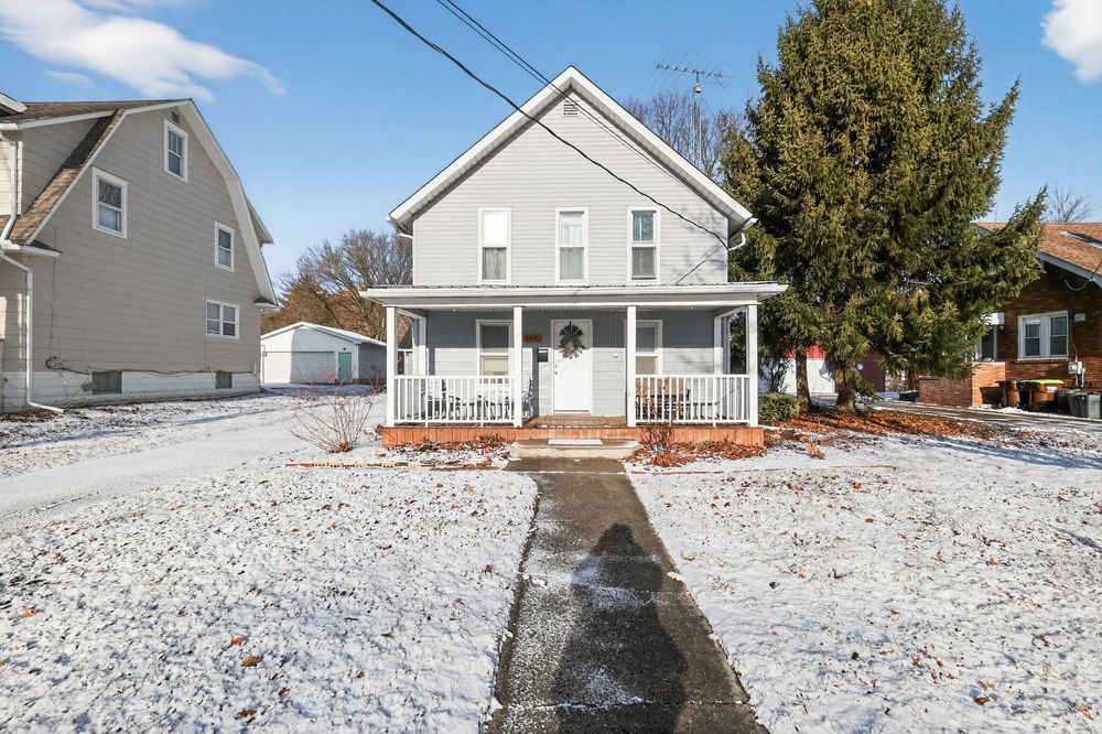 Two-story gray home with covered front porch dusted in snow on a bright winter day.
