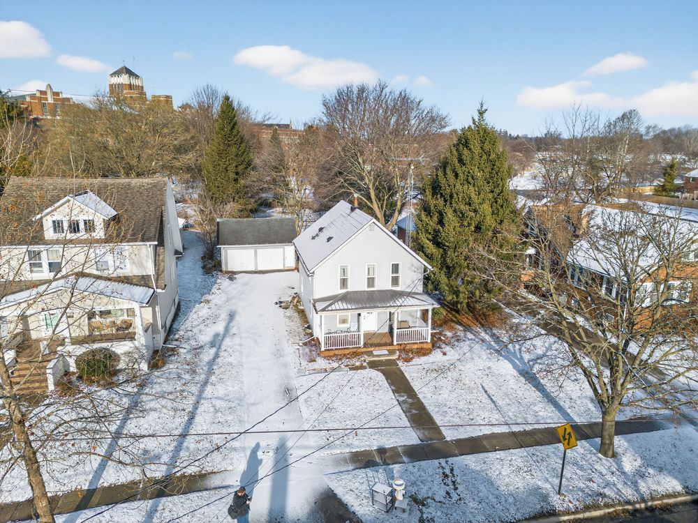 Aerial winter view of a white two-story home with snow-covered yard and neighboring houses in a residential neighborhood.