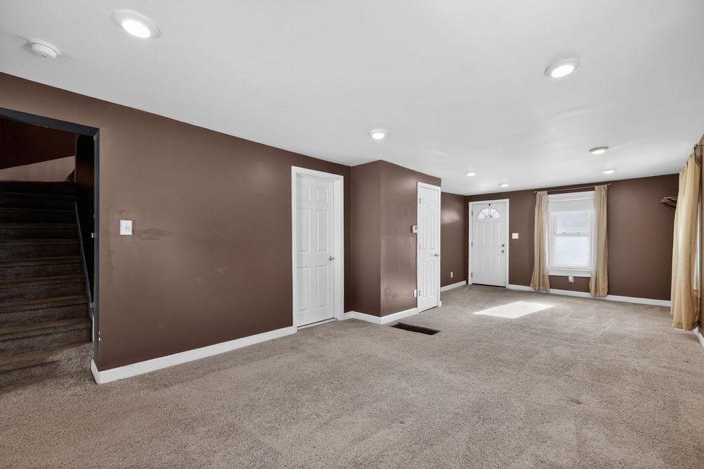 Spacious basement with brown walls, recessed lighting, neutral carpet, and multiple doors leading to utility areas.