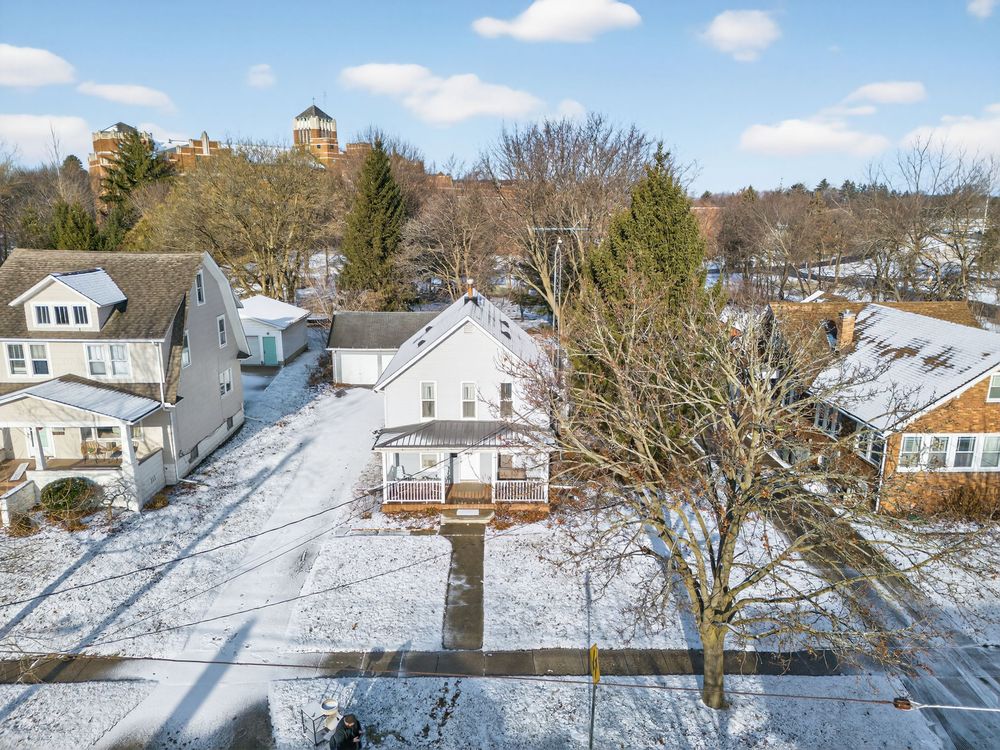 Aerial winter view of a white two-story home surrounded by snow-covered yards and bare trees.