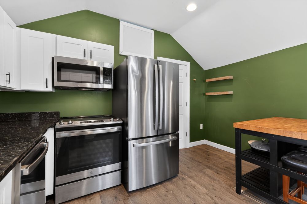 Modern kitchen with stainless steel appliances, white cabinets, dark granite countertops, and bold green accent walls.