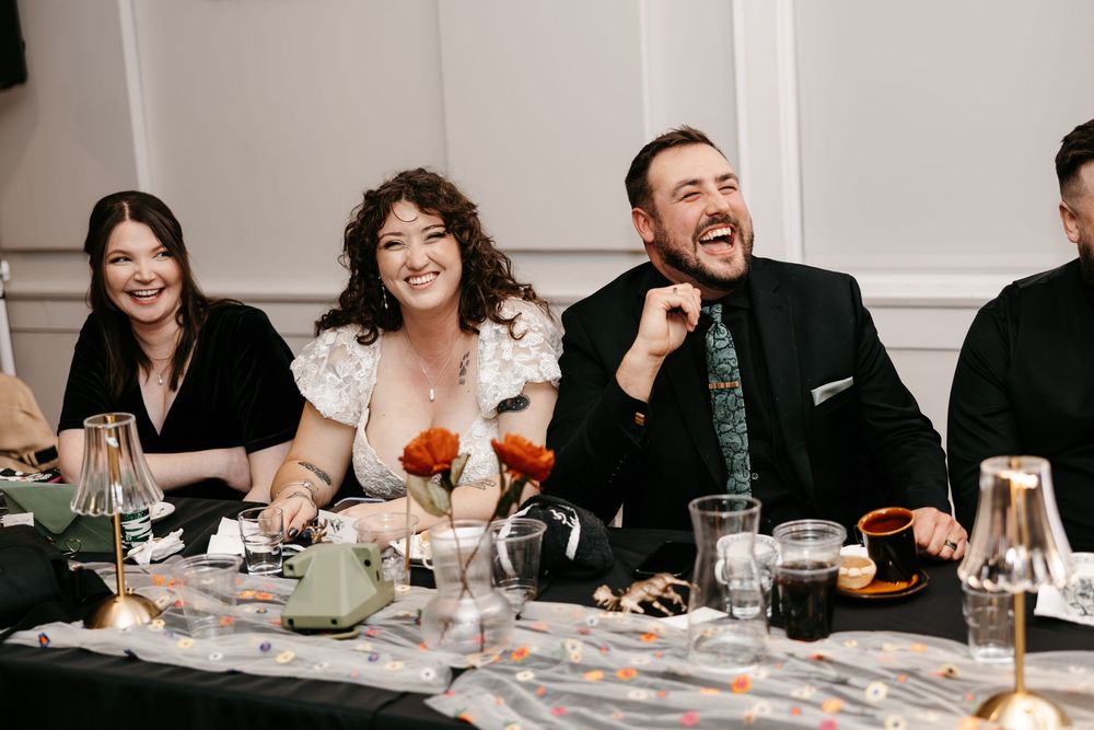Wedding guests share laughter and joy around a dinner table with wine glasses and place settings at a reception.