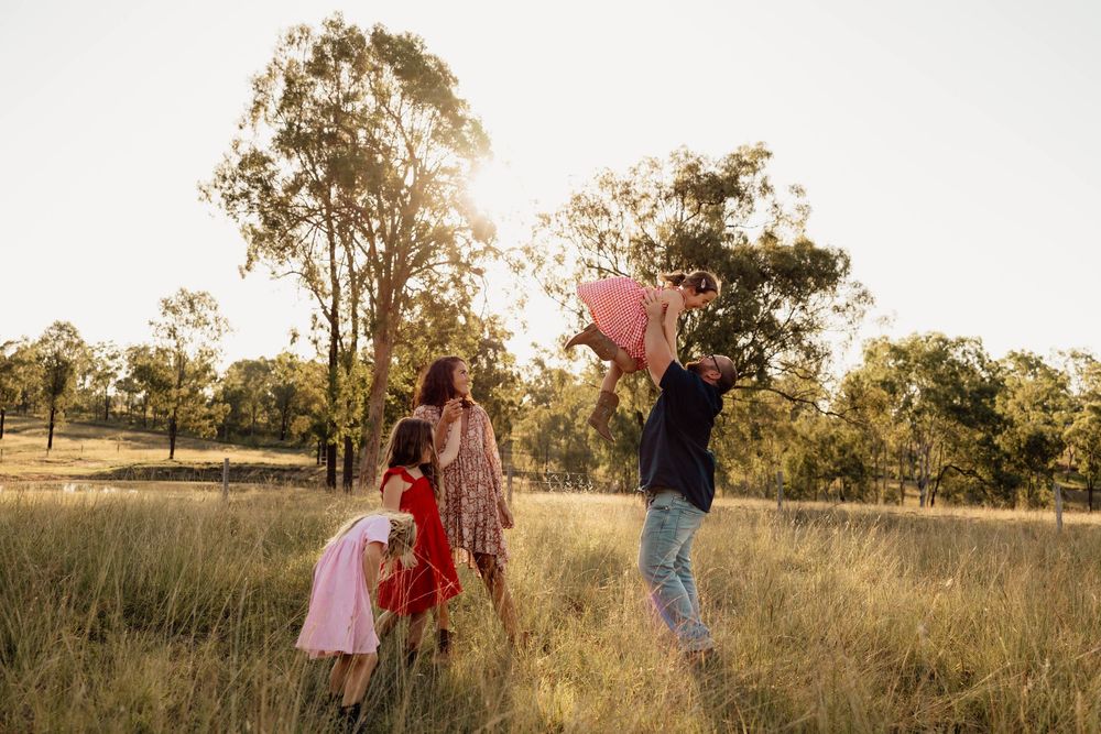 Family playing outdoors in a sunlit field, with father lifting child in the air at golden hour.