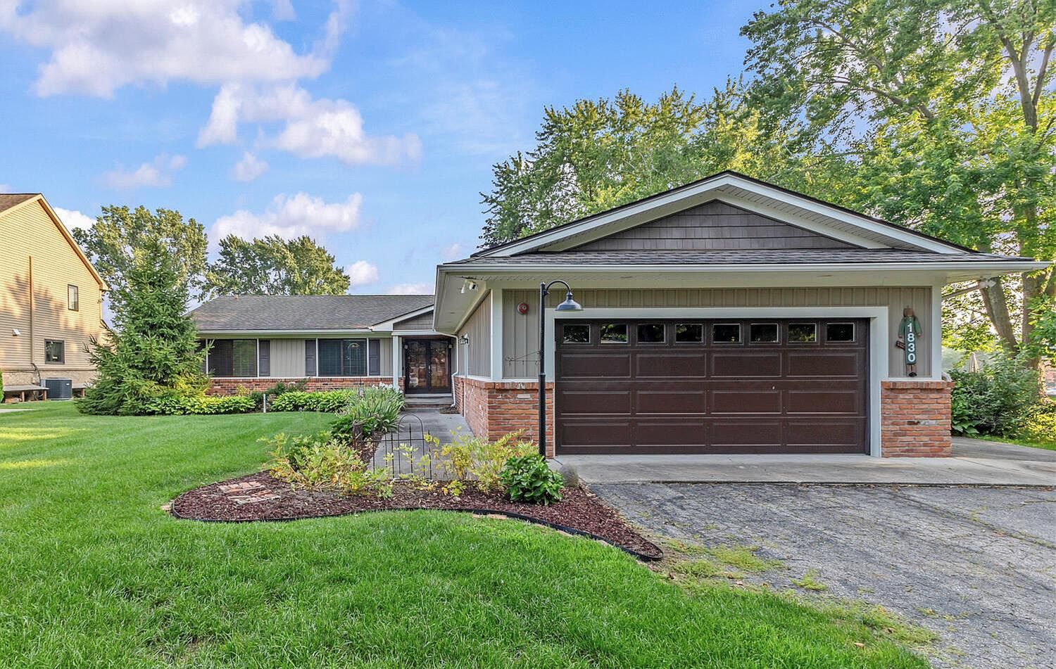 Ranch-style brick home with two-car garage, manicured lawn, and mature trees in a suburban setting.