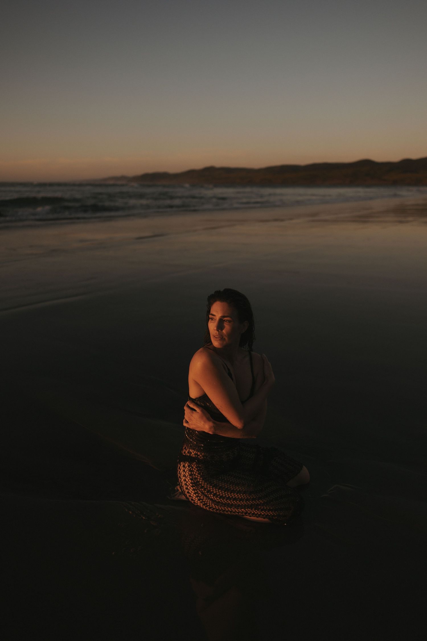 Woman sitting on wet sand at beach during dramatic golden hour sunset glow in New Zealand..