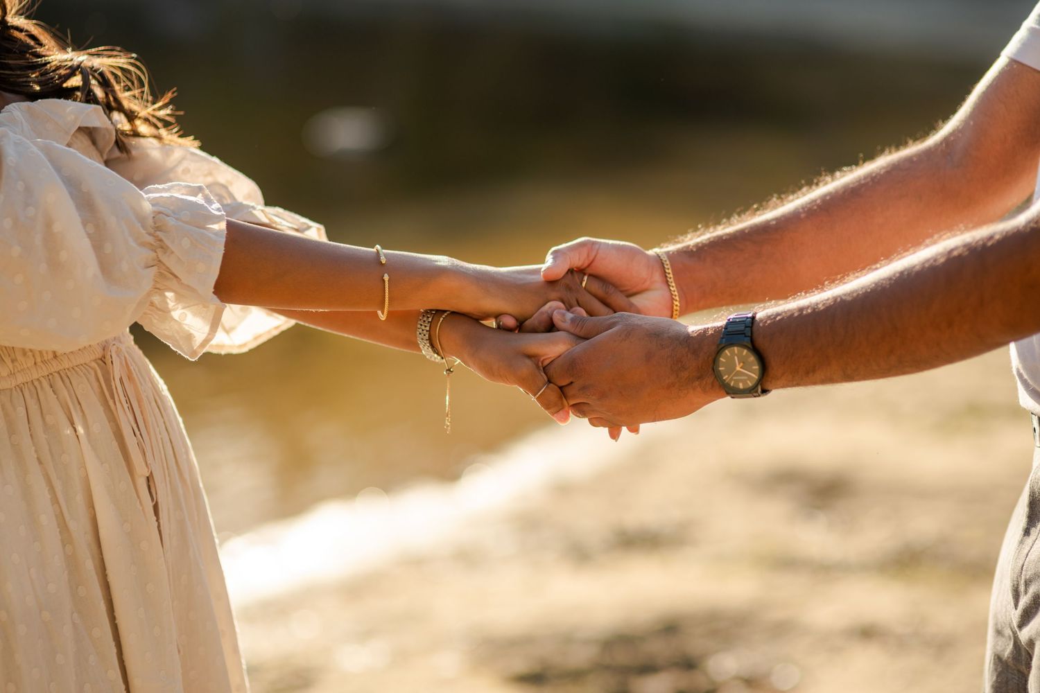 Adult and child holding hands outdoors in warm golden sunlight near water, symbolizing family bond and connection.