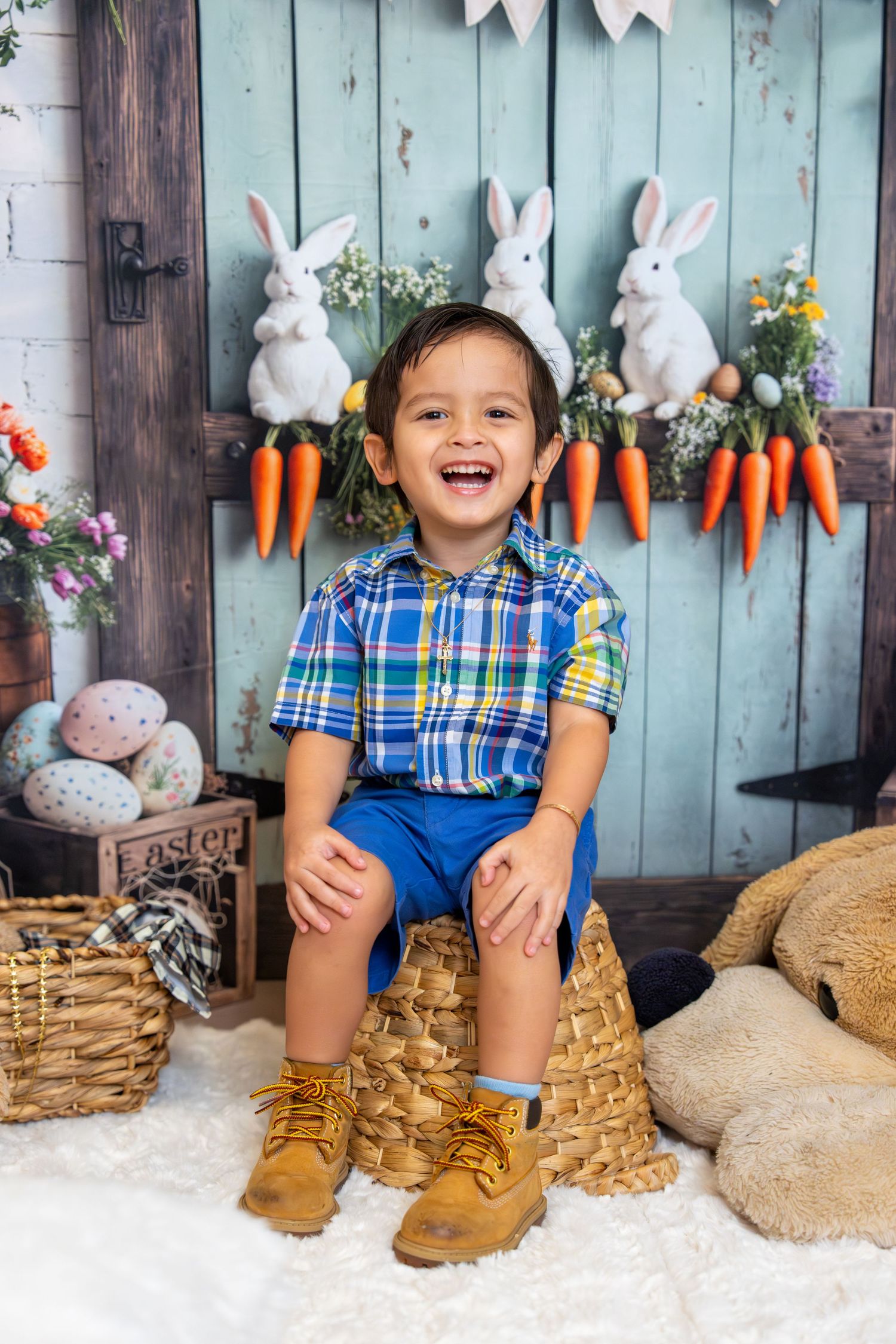 A joyful young boy sits in a basket amid Easter decorations with bunnies, carrots, and colorful eggs.