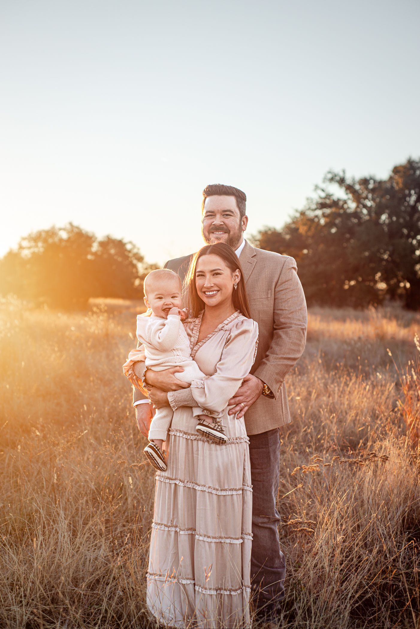 Family portrait in a golden field at sunset with warm lighting.