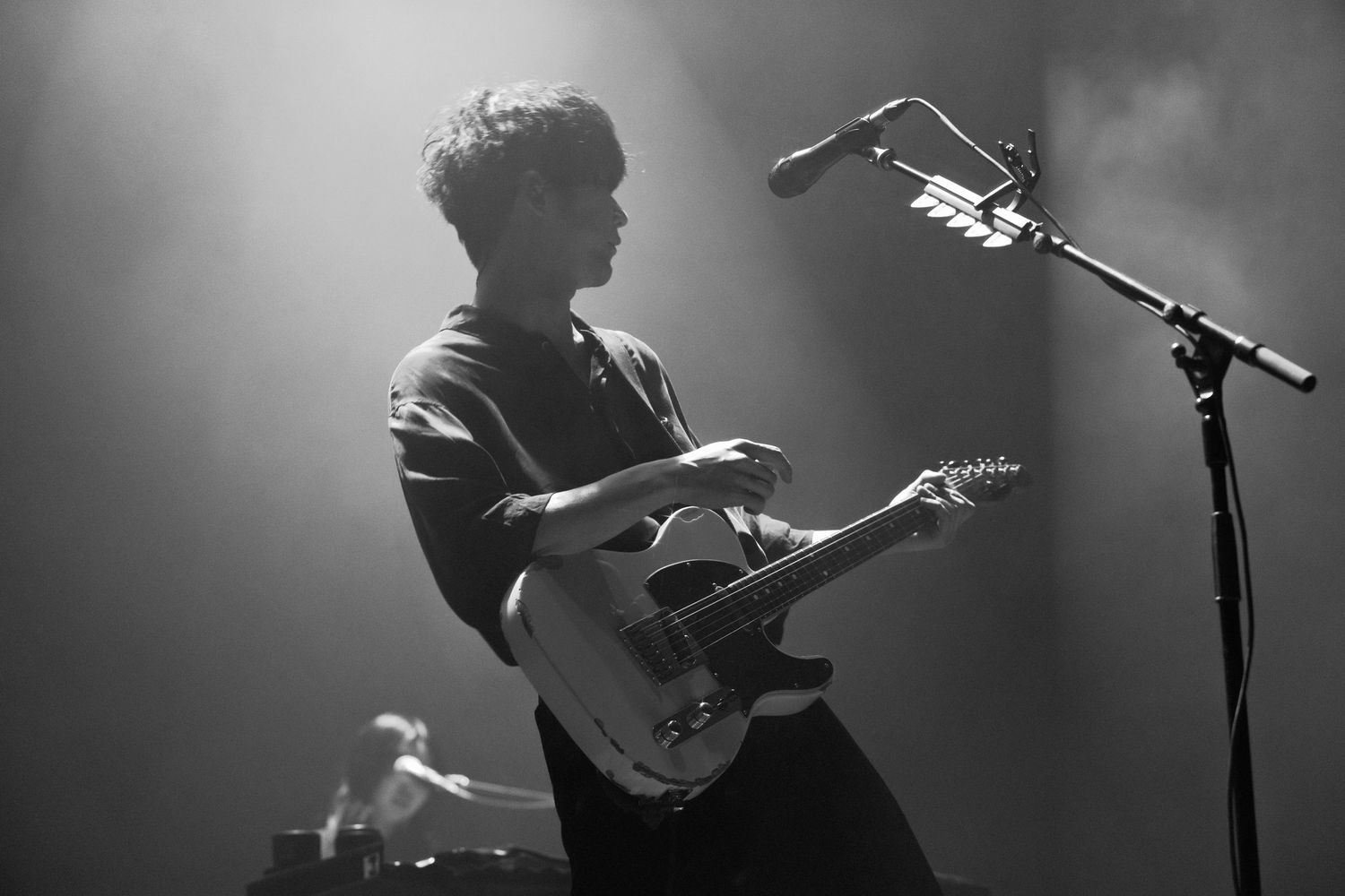 Black and White photo of TK from Ling Tosite Sigure strumming his guitar on stage at his concert at the Belasco. Concert lights on stage.
