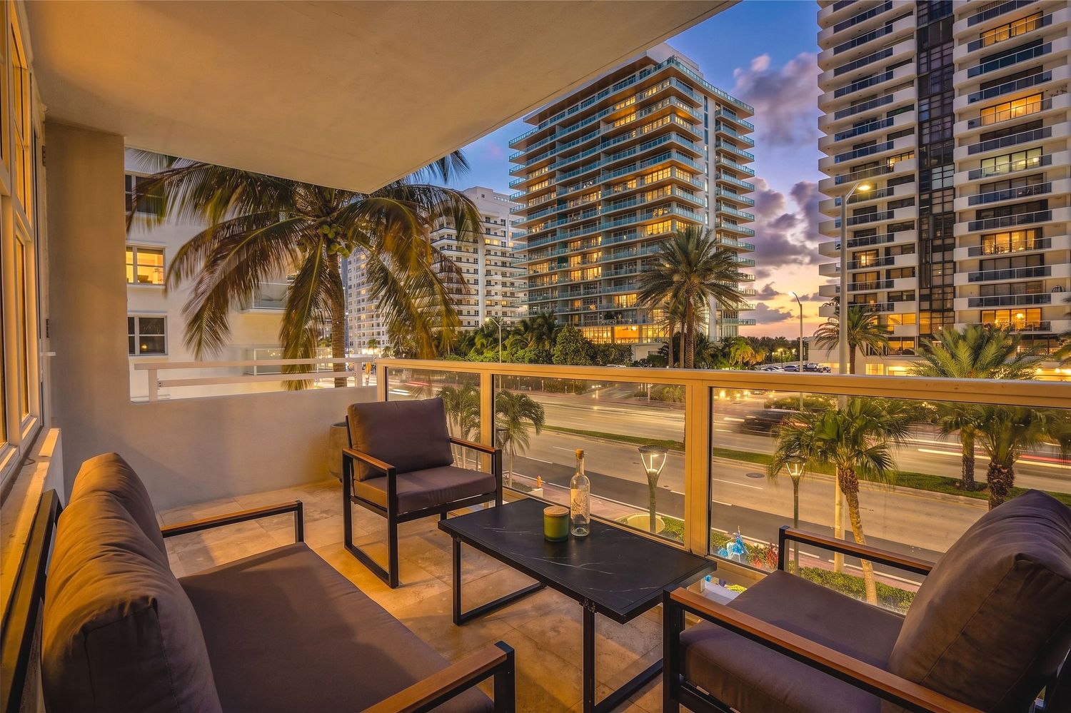 Luxurious balcony with outdoor seating overlooking Miami high-rise buildings and palm trees at sunset.