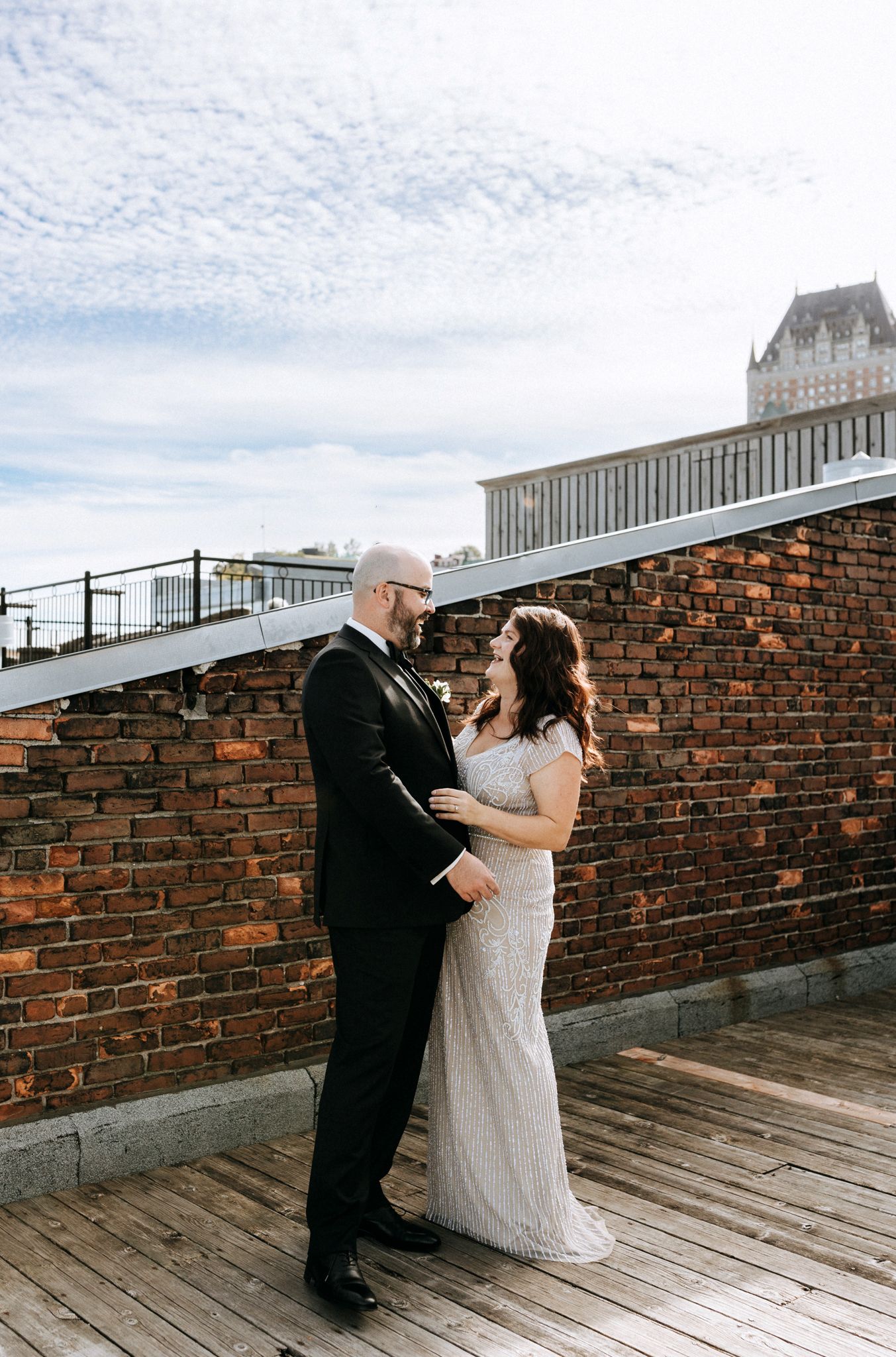 A couple shares a moment on a rooftop terrace with brick walls and city views.