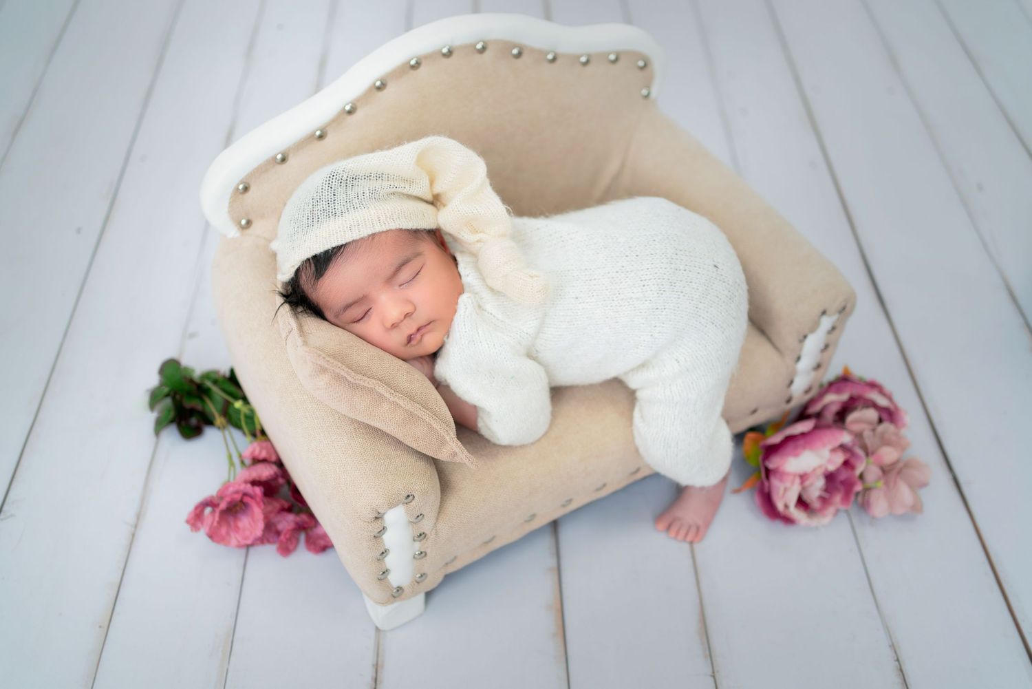 Newborn baby sleeping on mini sofa wrapped in white cloth, studio photoshoot