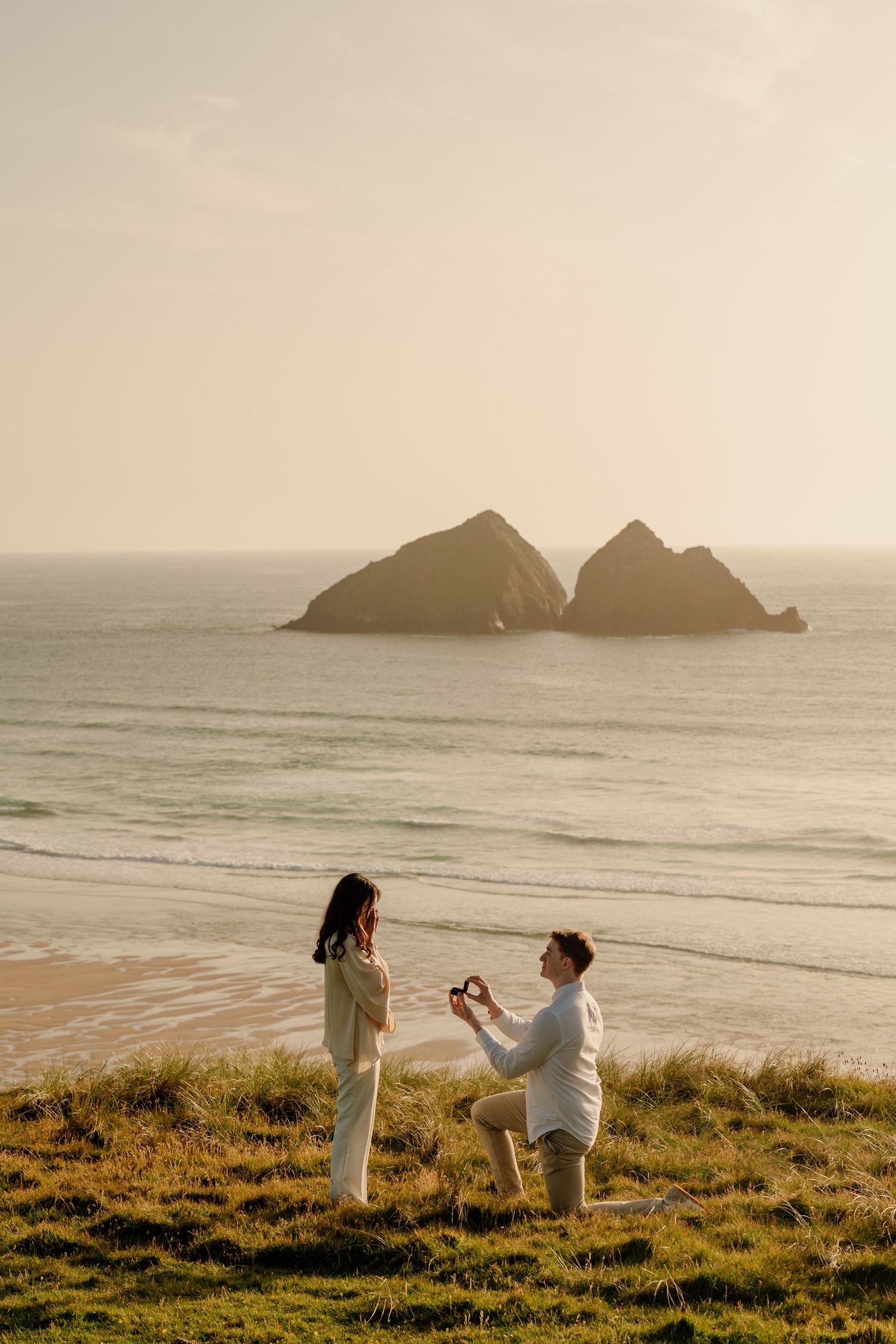Man proposing to woman on the cliffs overlooking Holywell Bay at sunset.