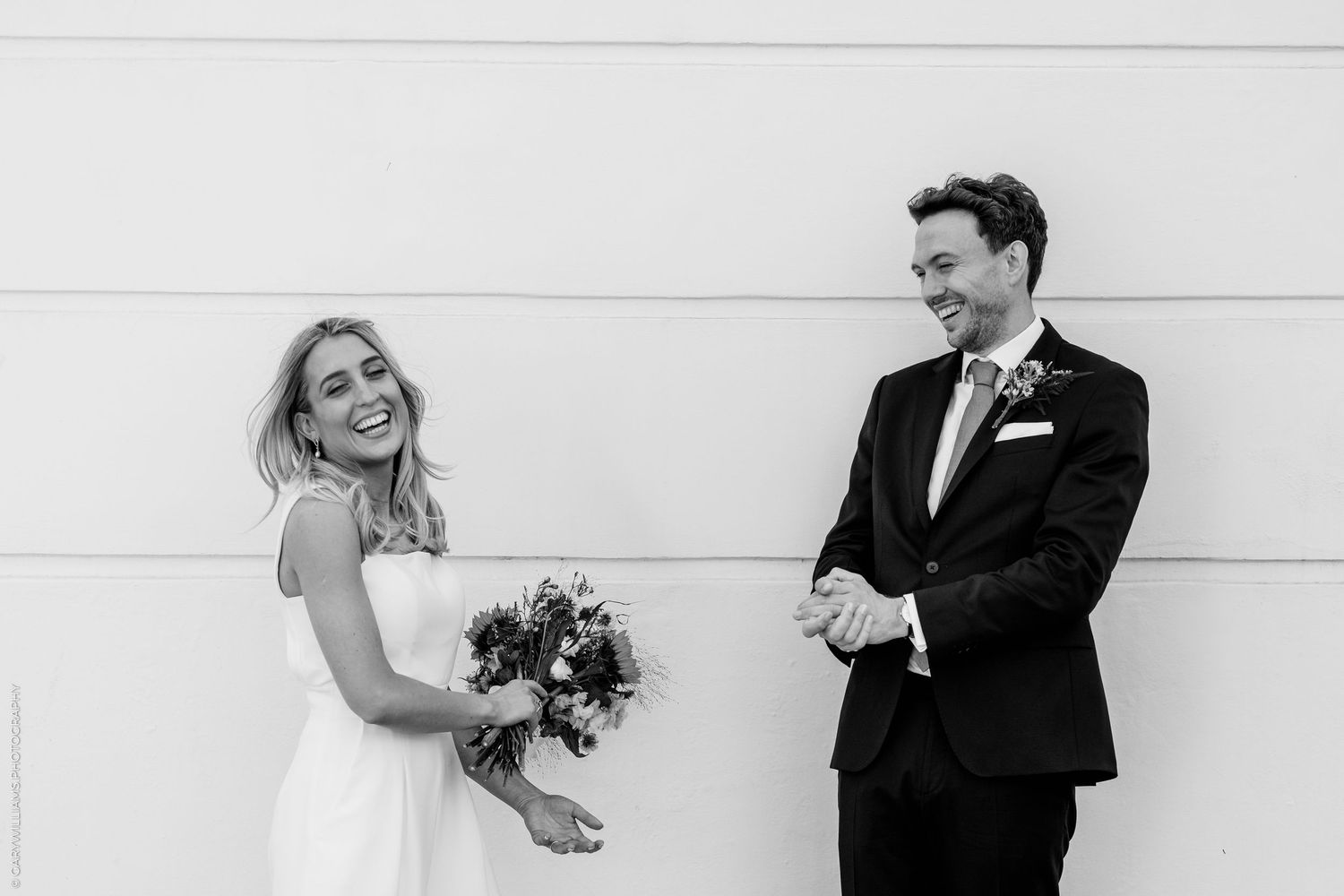 Bride and groom exit under a stunning floral arch surrounded by guests throwing confetti at an outdoor wedding celebration.