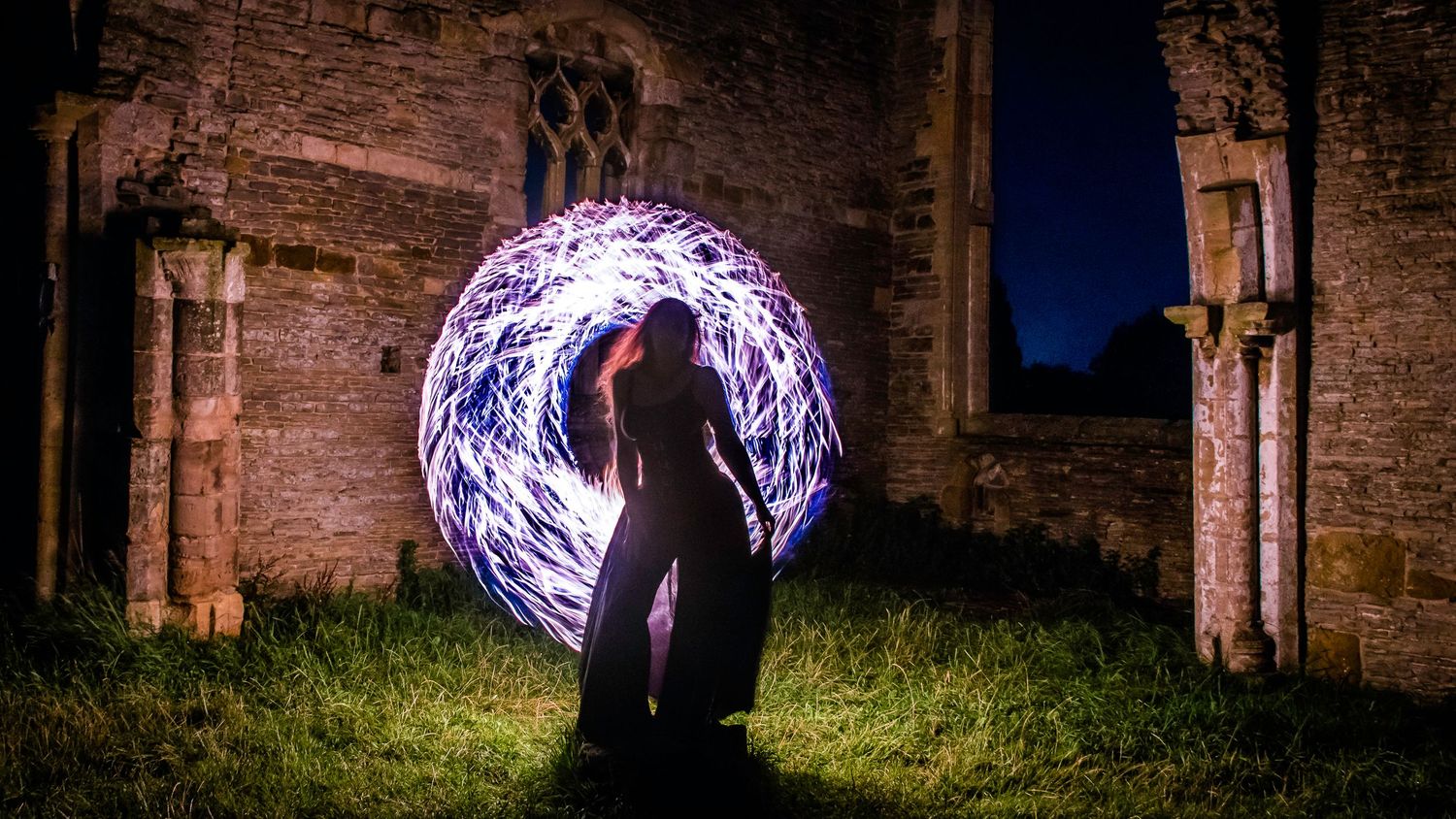 Person standing before glowing purple light orb at ancient stone ruins at night, creating magical long exposure photography effect.