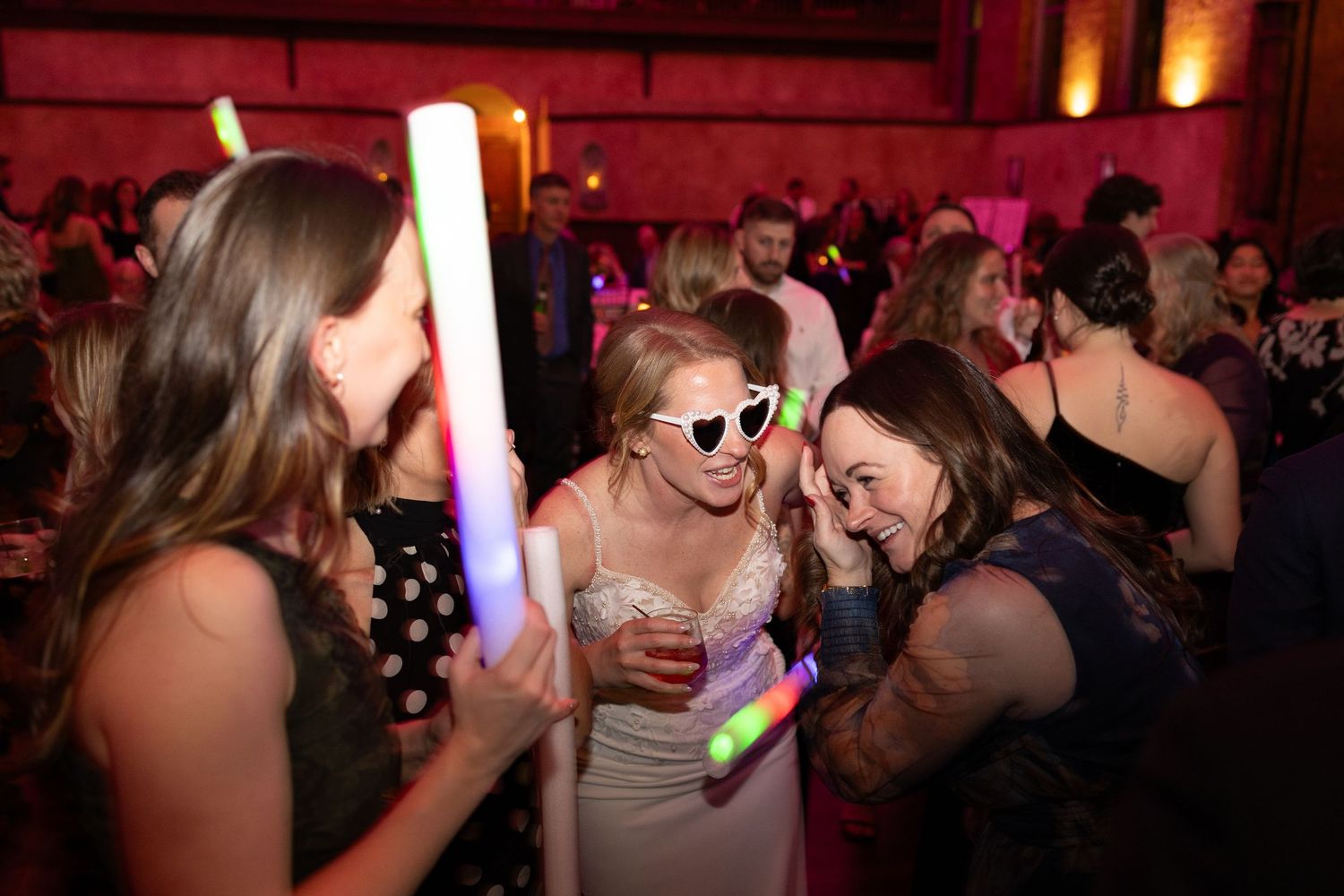 Bride celebrating at her wedding reception party with glow sticks and heart-shaped sunglasses on the dance floor.
