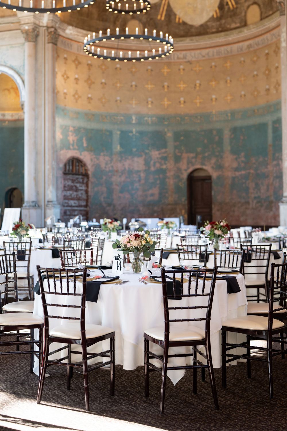 Elegant wedding reception in the historic Monastery with round tables, chiavari chairs, floral centerpieces, and ornate domed ceiling.
