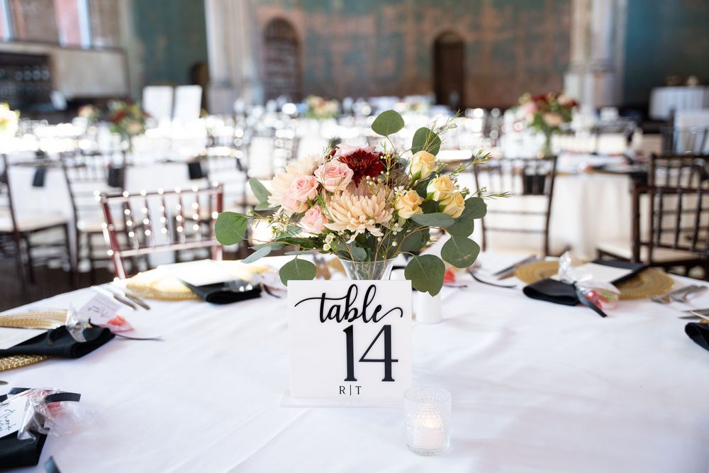 Elegant wedding reception table 14 centerpiece with pink and burgundy roses, eucalyptus greenery, and gold accents.