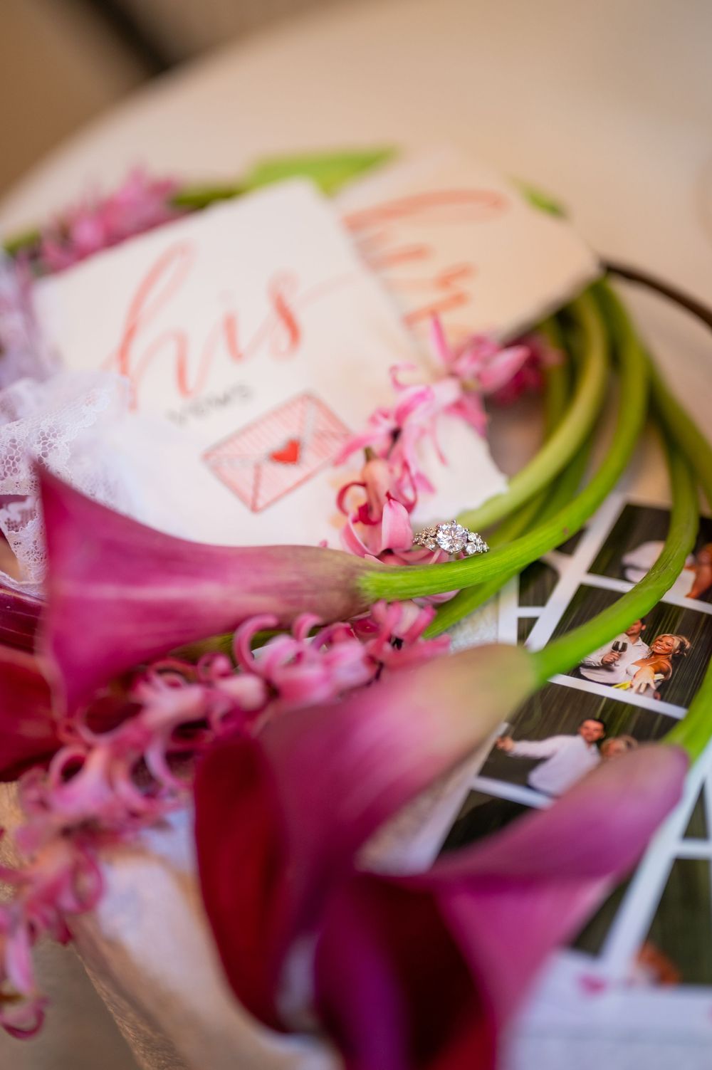 Pink calla lilies and hyacinths surround wedding stationery and a diamond engagement ring in an elegant bridal flat lay.