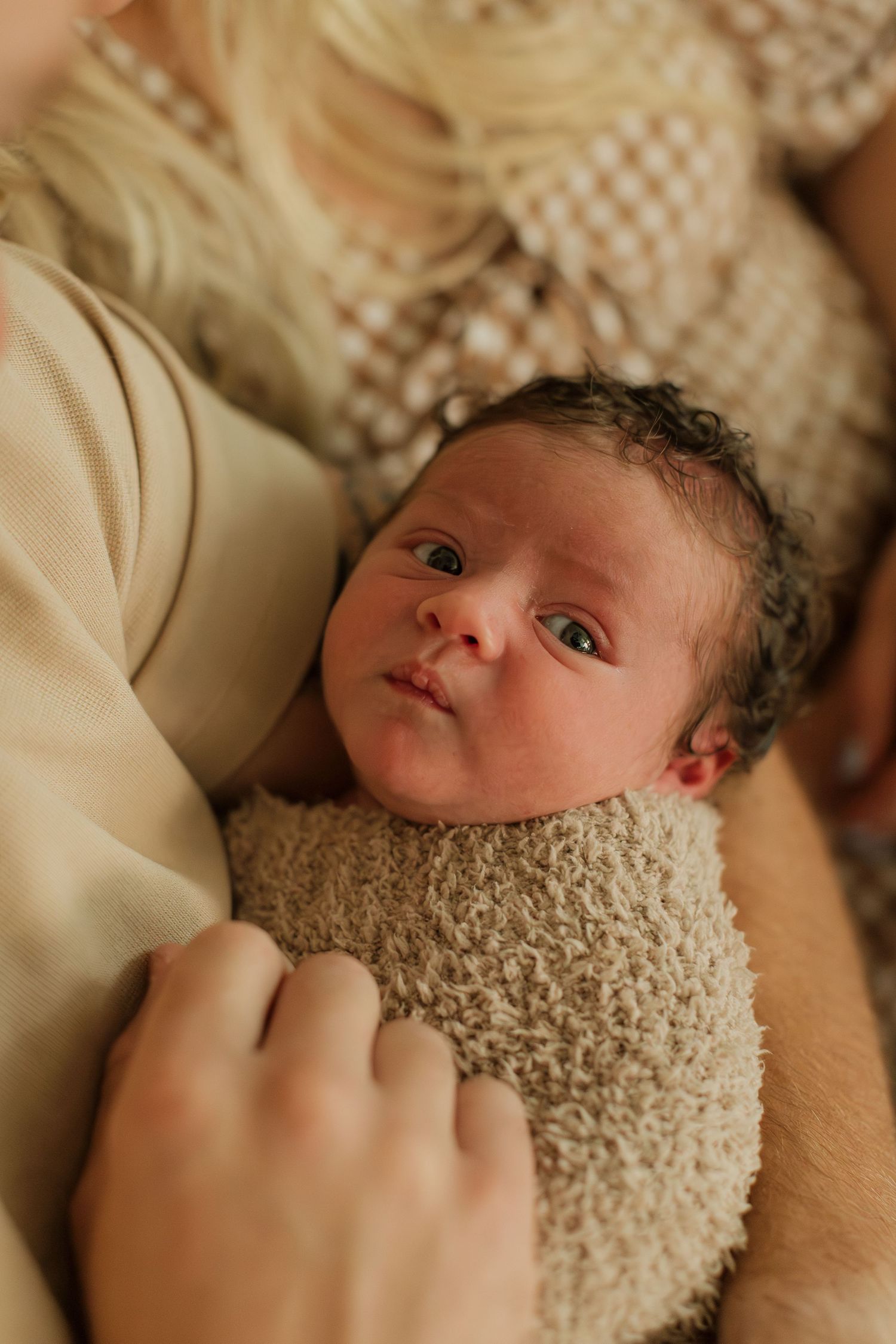newborn baby with wide eyes held by mom