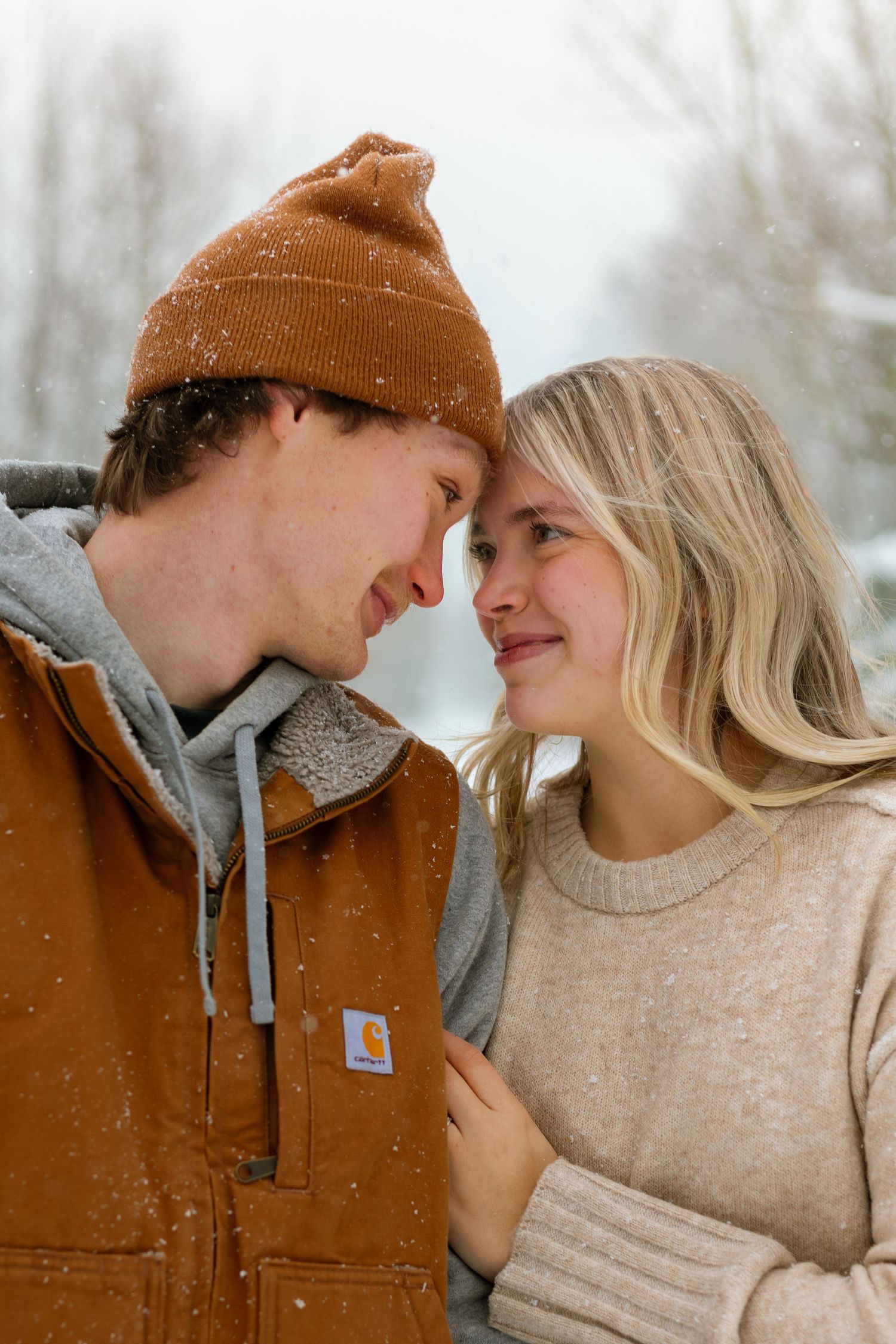 Young couple sharing a romantic moment in the snow, wearing Carhartt winter clothing outdoors.